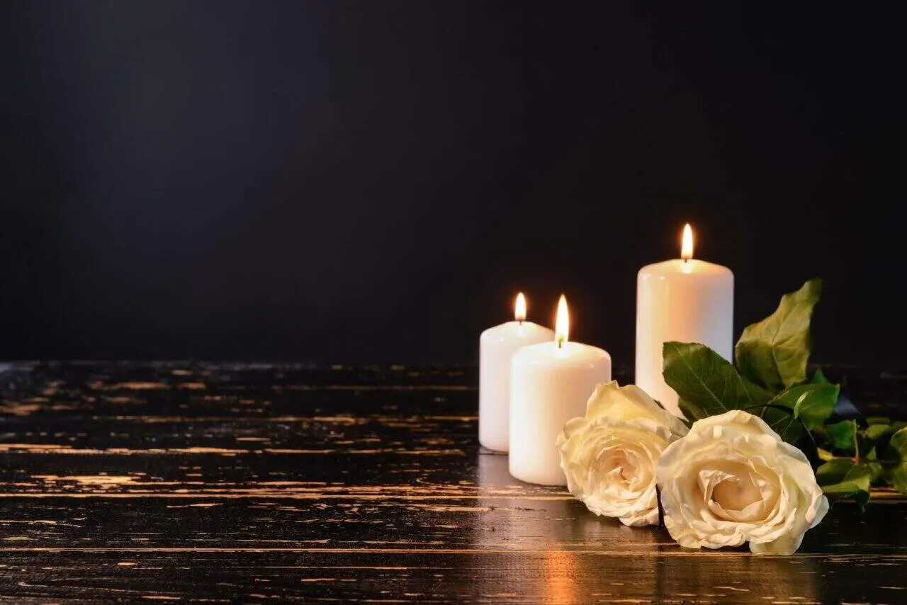 Burning candles and flowers on table against black background
